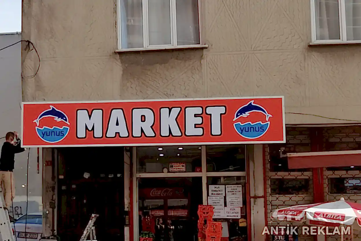 Market vinil baskılı cephe tabelası kırmızı zemin beyaz yazı yunuslu logo dış mekan uygulaması